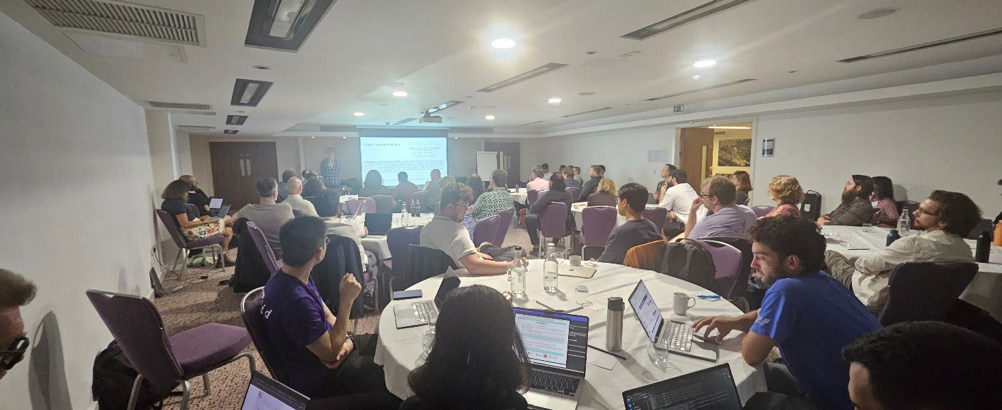 AI Conference 2025: Participants sat around circular tables looking at a projector screen